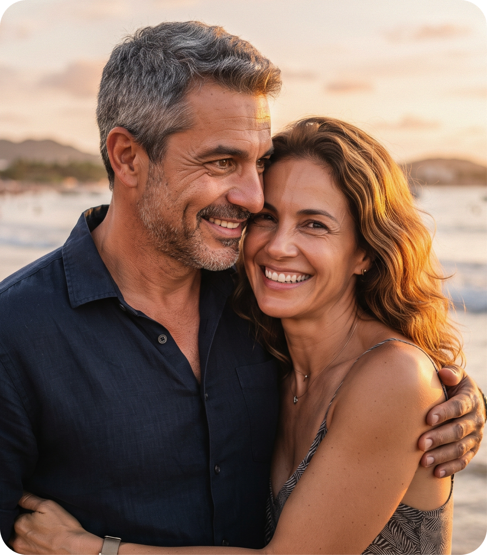 Casal sorridente abraçado na praia ao pôr do sol
